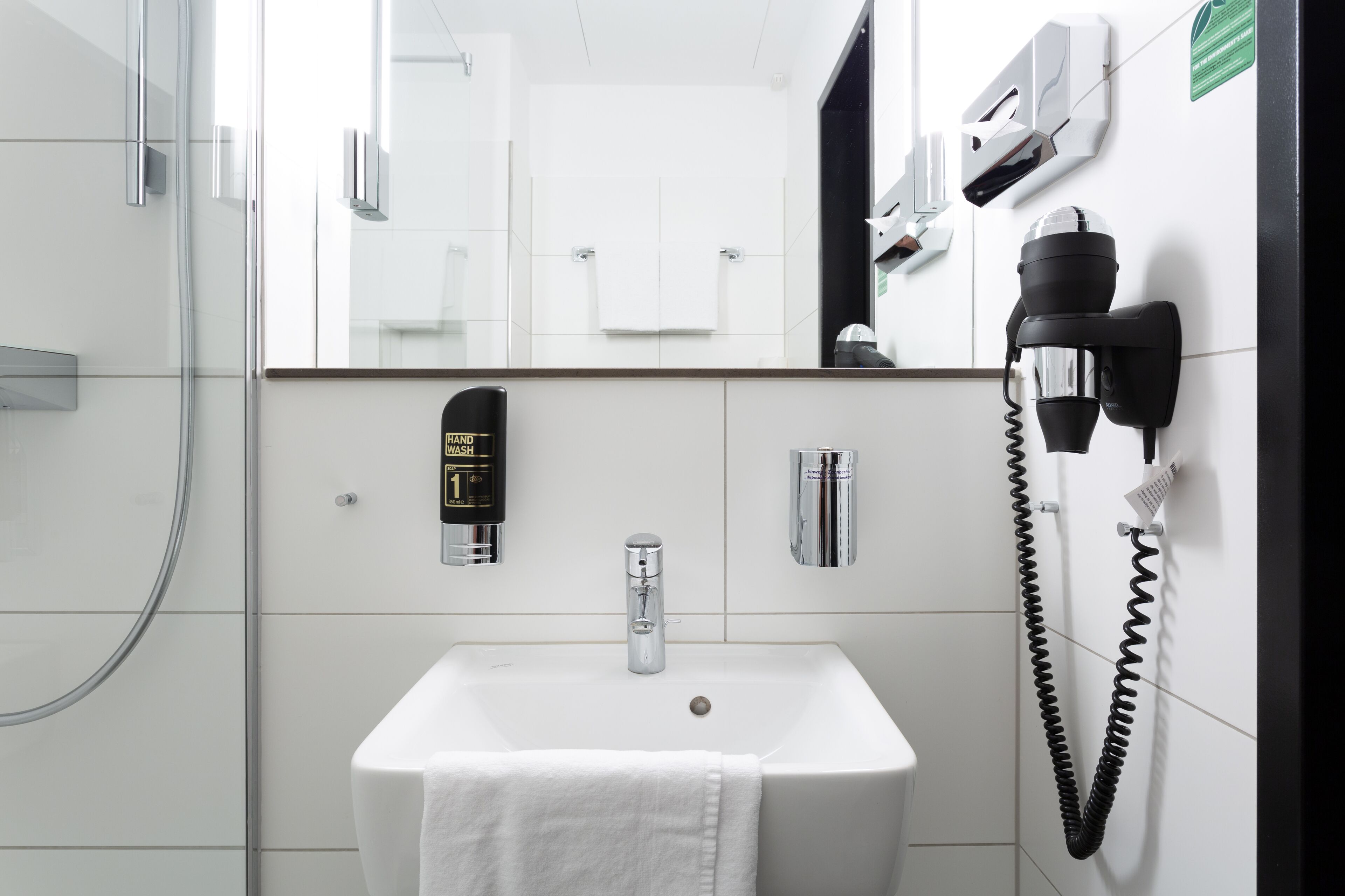 Un bagno moderno con un lavandino bianco, un soffione a mano, un asciugacapelli e uno specchio.