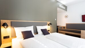 Una habitación de hotel moderna con una cama grande, lámparas de noche, un cabecero de madera y un escritorio pequeño con una silla.