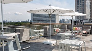 Una terraza en la azotea con mobiliario exterior, sombrillas y vistas del horizonte de la ciudad.
