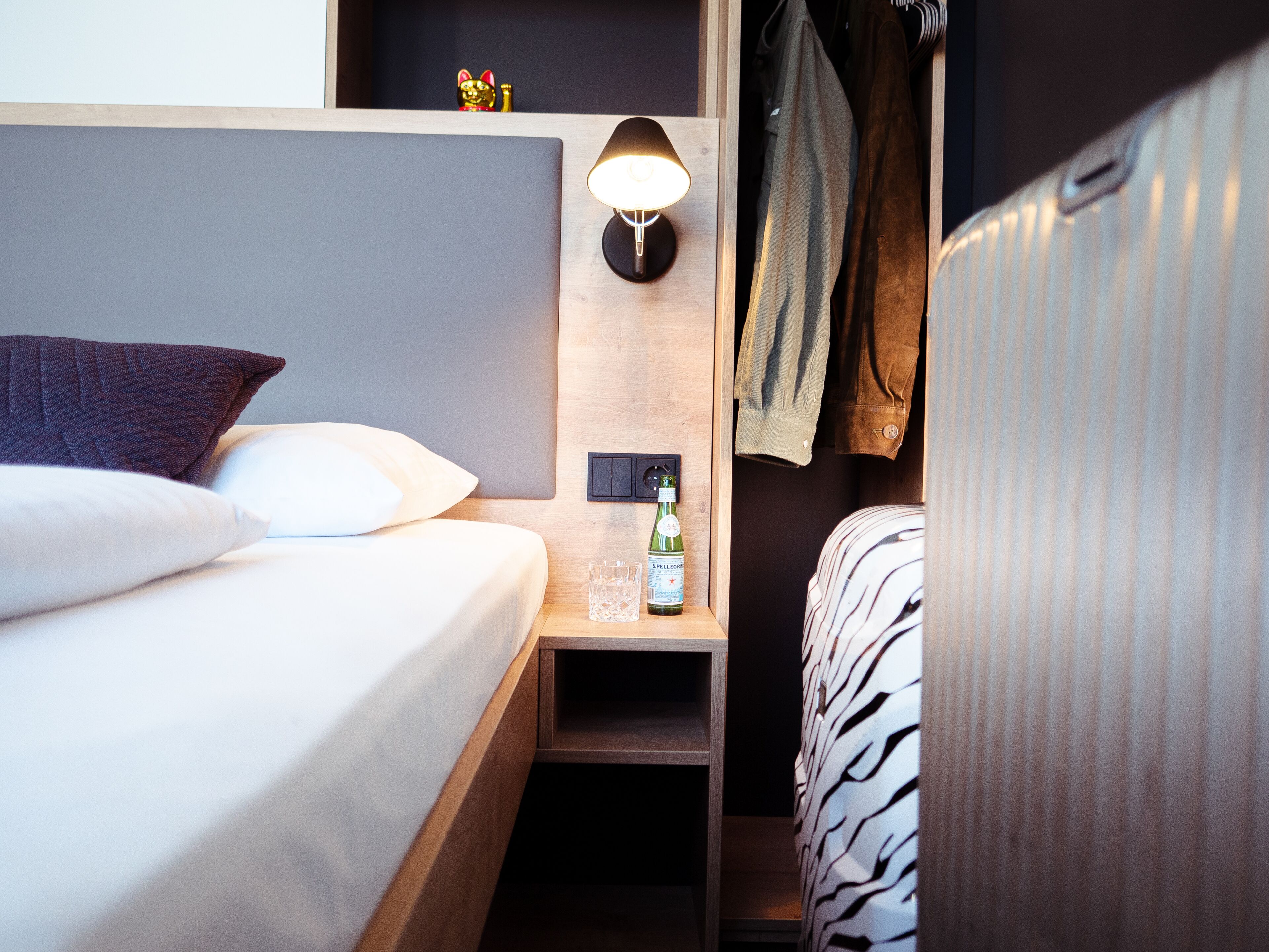 A neatly made bed with a pillow and a bedside table with a bottle and glass.