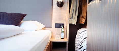 A neatly made bed with a pillow and a bedside table with a bottle and glass.