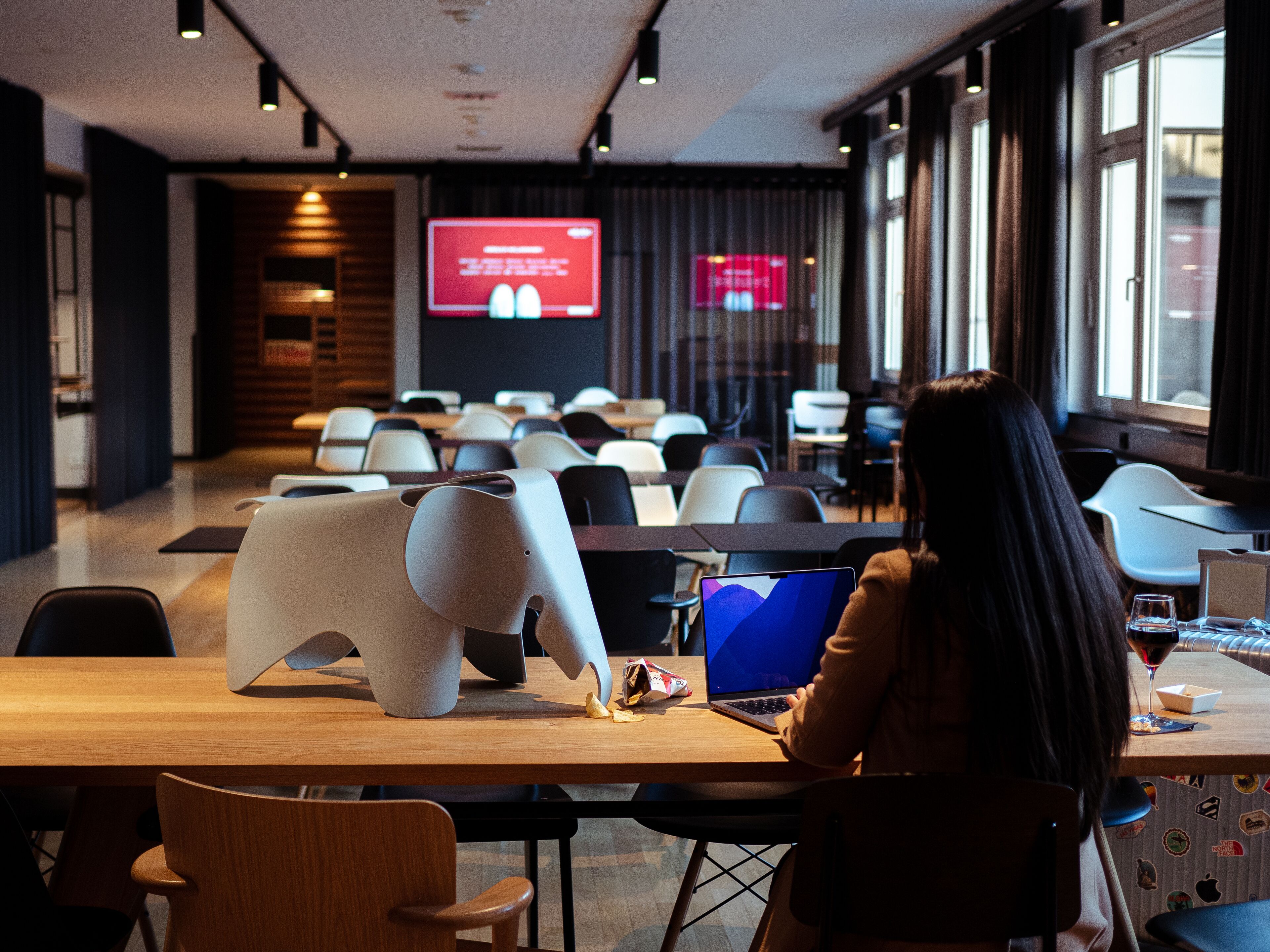 A modern conference room with a large screen displaying a presentation, rows of chairs, and a laptop on a table.