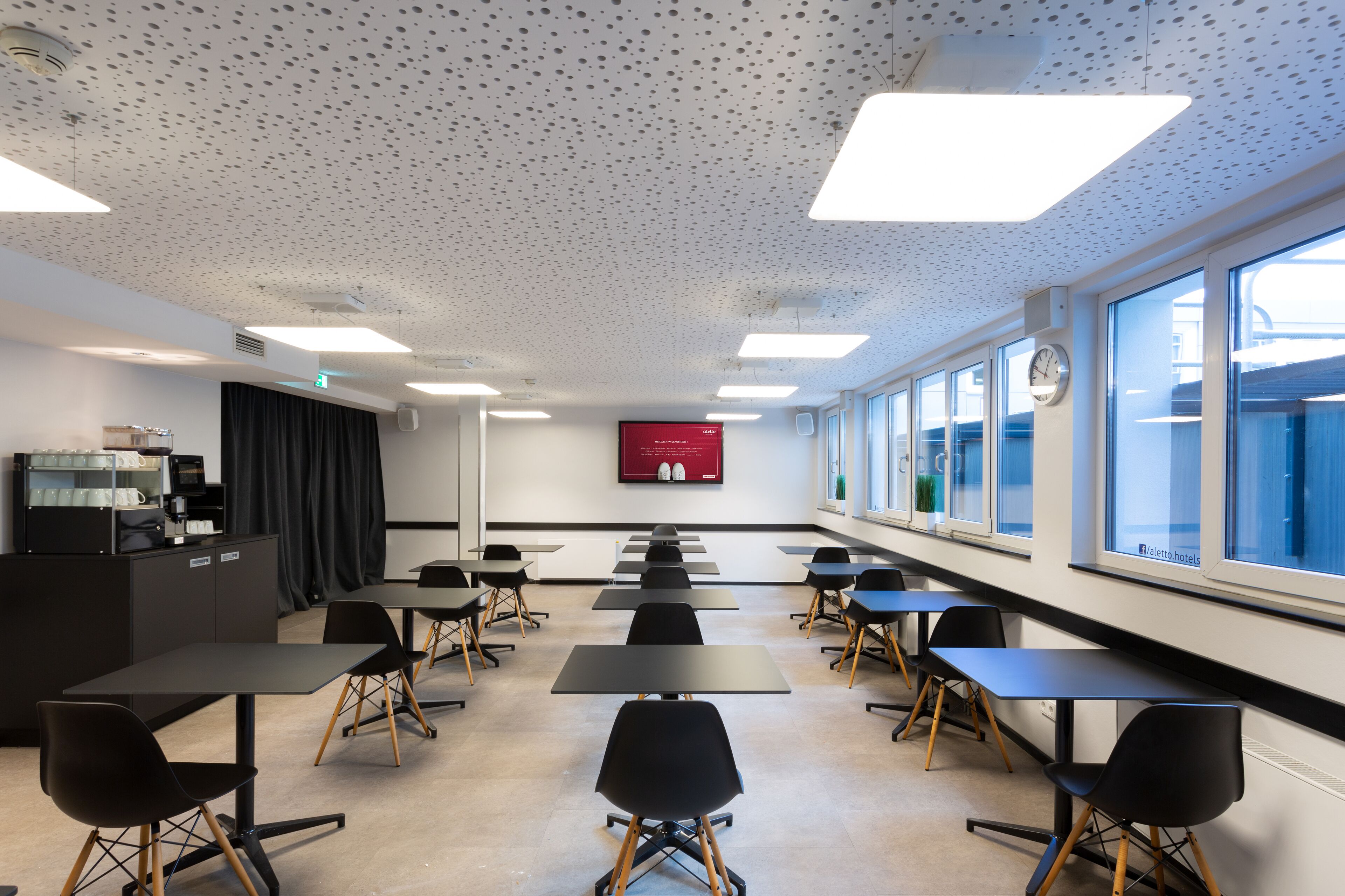 A conference room with tables and chairs, a projector screen, and a coffee machine.