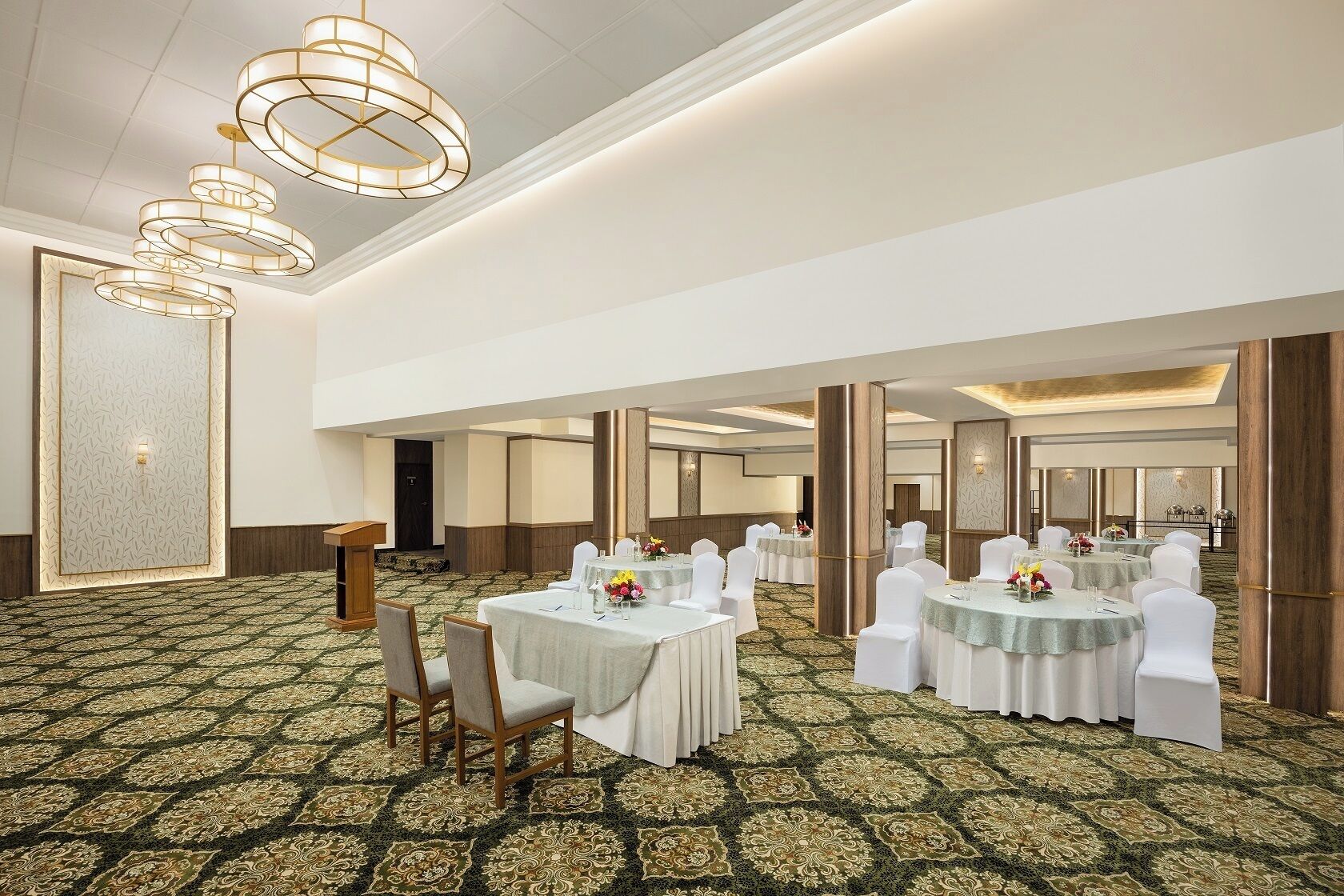 A spacious banquet hall with round tables, white chairs, and a patterned carpet.