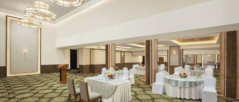 A spacious banquet hall with round tables, white chairs, and a patterned carpet.