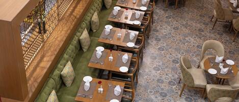 A restaurant with a long green sofa and multiple dining tables, each set with white plates and silverware.