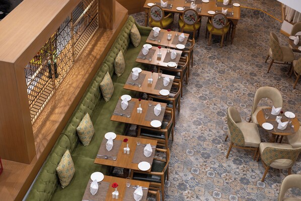 Un restaurante con un sofá verde largo y varias mesas de comedor, cada una con platos y cubiertos blancos.