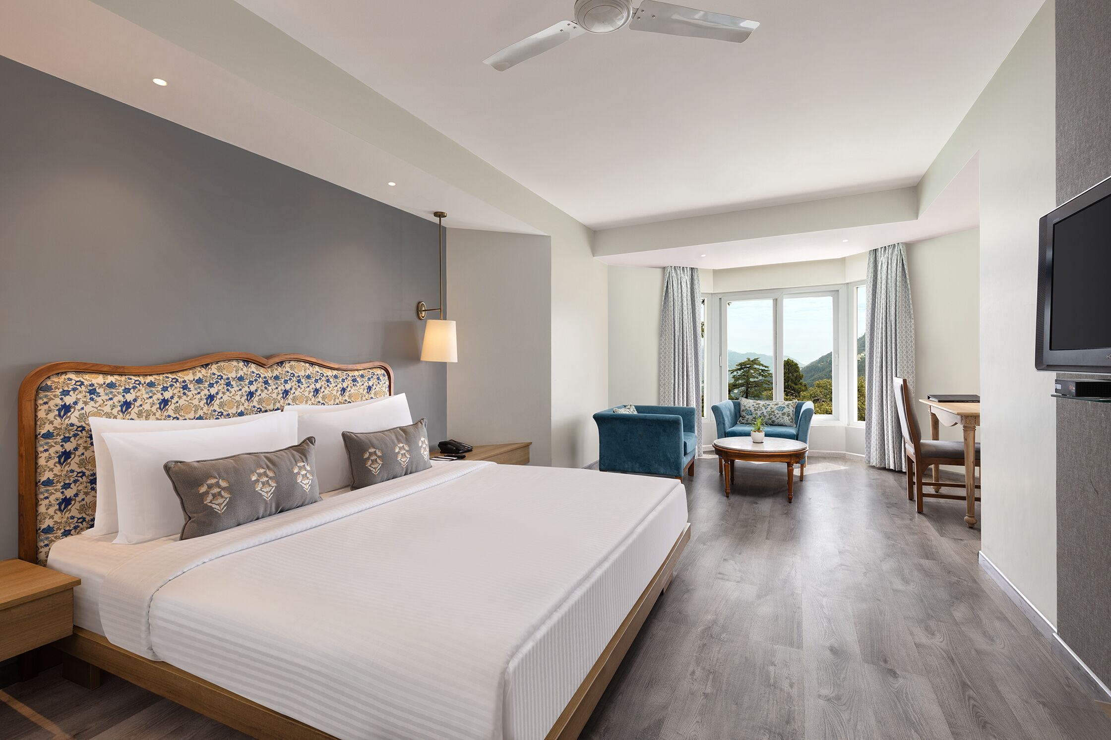 A modern hotel room with a large bed, a desk, a chair, and a TV.