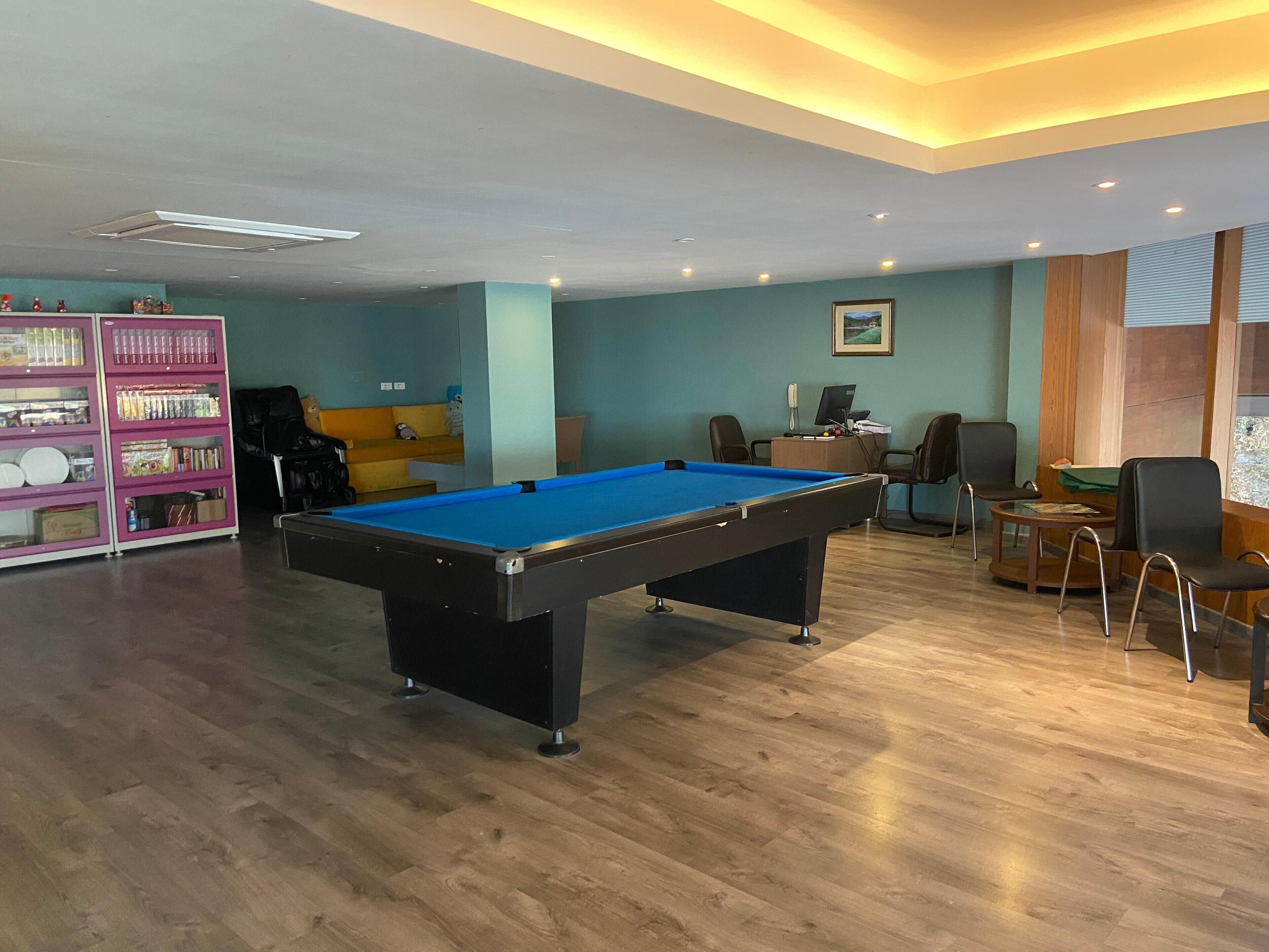A pool table in a room with a wooden floor, a sofa, and a desk with a computer.