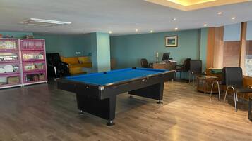A pool table in a room with a wooden floor, a sofa, and a desk with a computer.
