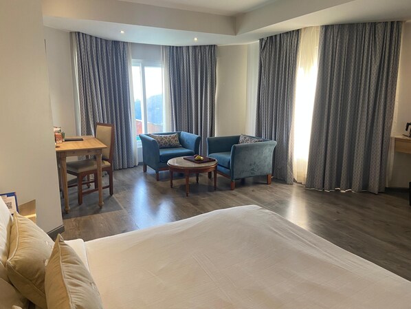 Una habitación de hotel con una cama grande, un escritorio con una silla, un sillón azul y una mesita redonda.