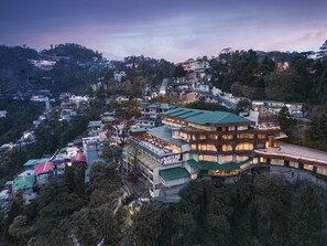 A multi-story building with a green roof, surrounded by trees and other buildings. - Fortune Resort Grace, Mussoorie  - Member ITC Hotels' Group (Dehradun)