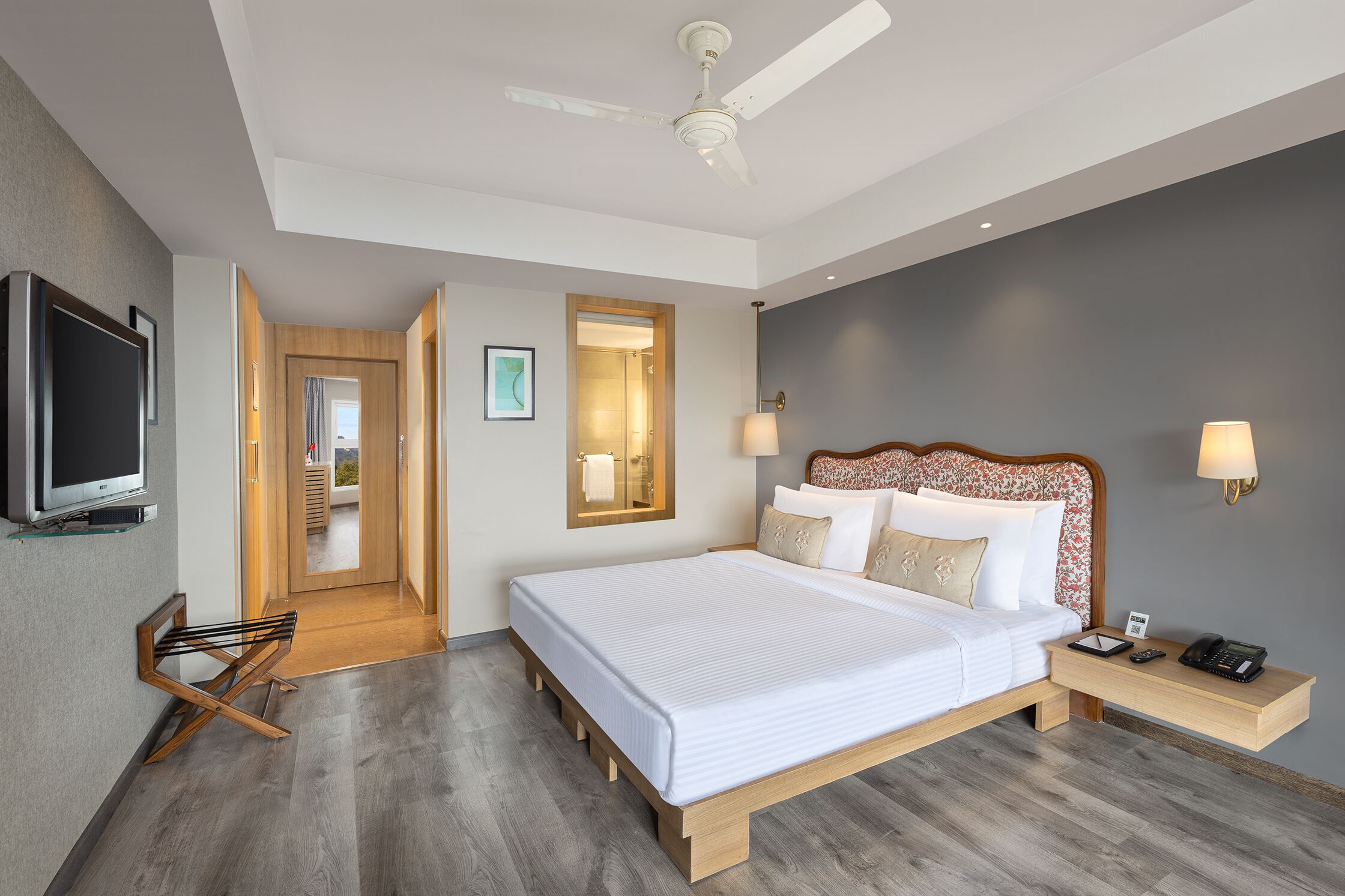 A modern hotel room with a large bed, a ceiling fan, a TV, and a wooden nightstand.