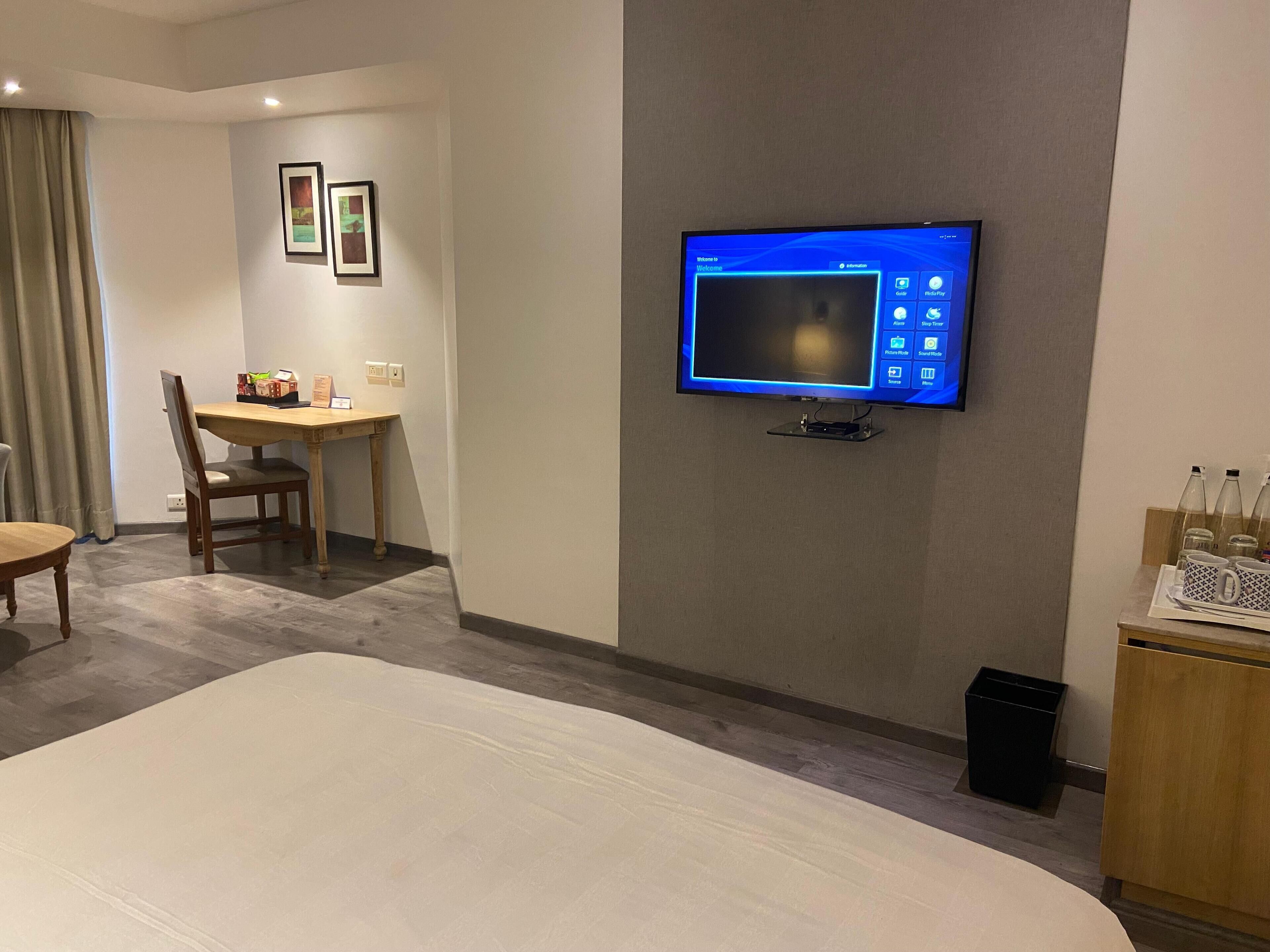 Habitación de hotel con una cama grande, un escritorio con silla, un televisor fijado a la pared y un cubo de basura pequeño.