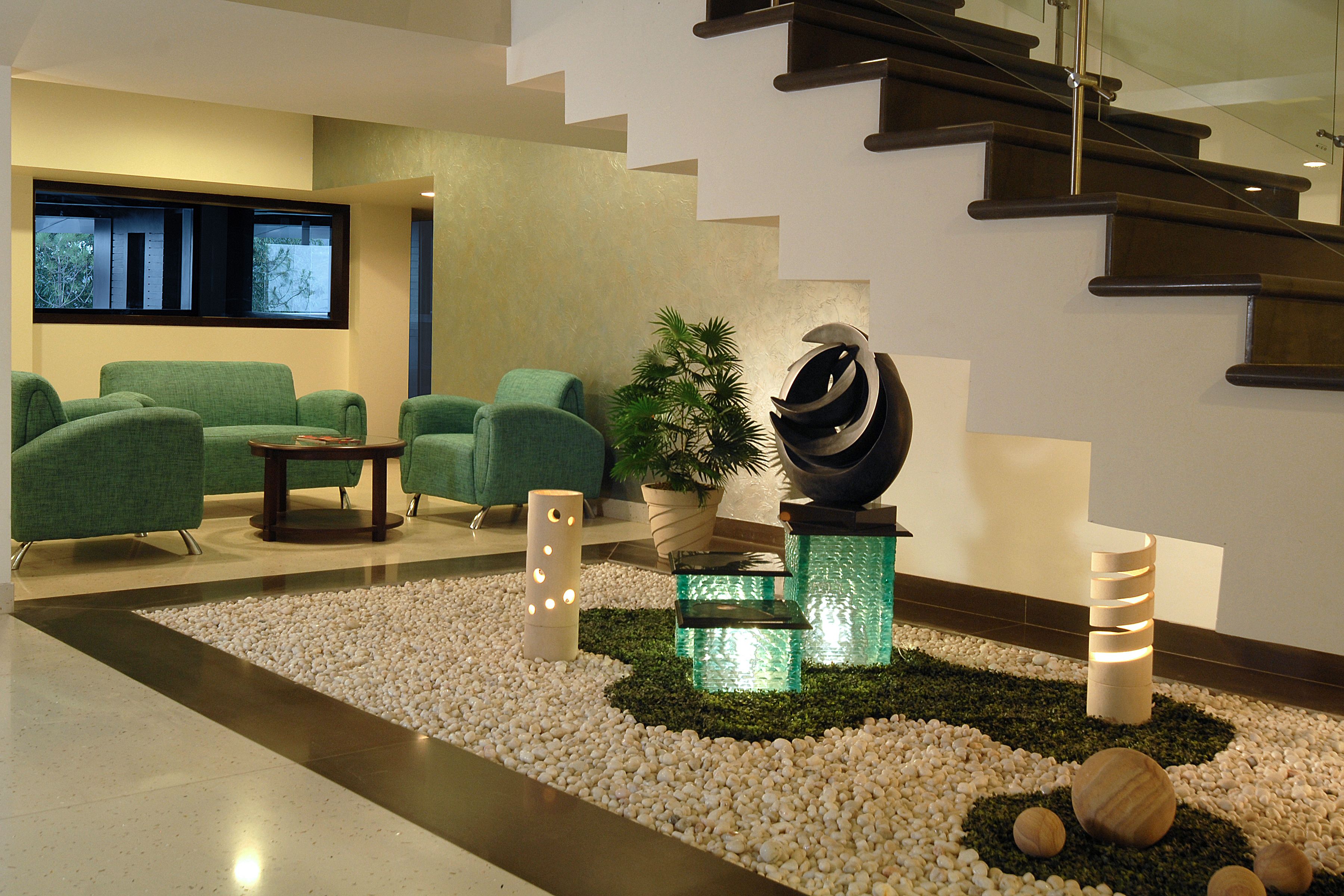 A modern lobby with green sofas, a glass coffee table, a decorative plant, and a staircase.