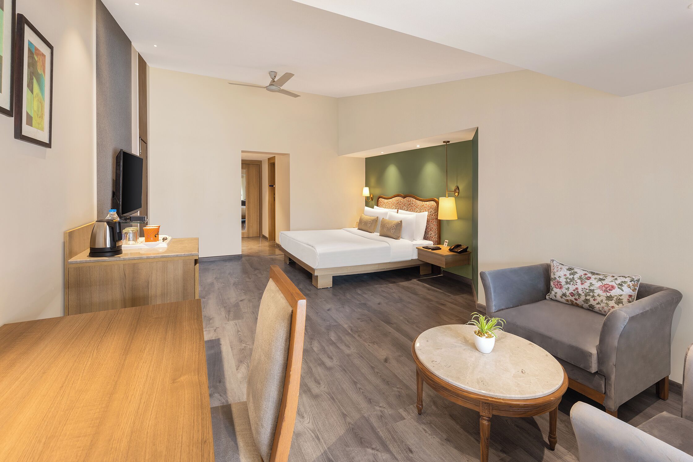 A hotel room with a bed, a sofa, a dining table, and a TV.