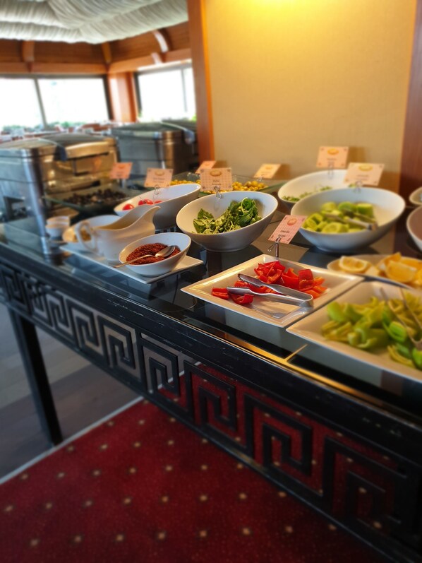En buffet med et udvalg af madmuligheder, herunder salater, frugt og en kaffestation.