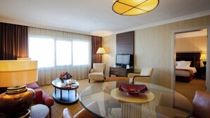 Een hotelkamer met een glazen salontafel, leren fauteuils, een televisie en een bed.