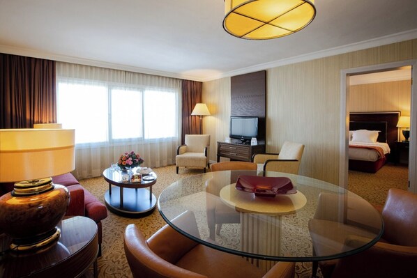 Habitació d'hotel amb una taula de cafè de vidre, butaques de cuir, televisió i un llit.