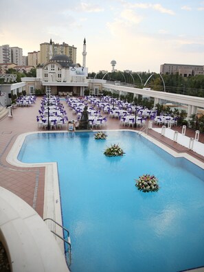 A rooftop pool area with multiple tables and chairs, surrounded by a pool with floating flower arrangements.