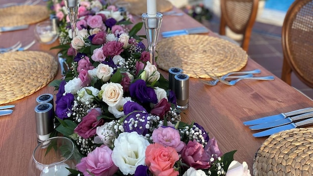 Une table à manger dressée pour un repas, avec vue sur la piscine, agrémentée d’un centre de table floral et de bougies.
