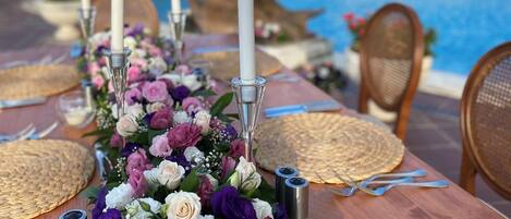 Una mesa de comedor preparada para una comida, con vista a una piscina, adornada con un centro de flores y velas.