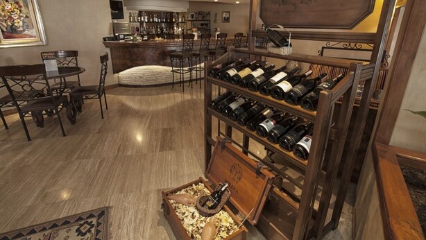 Een ruime kamer met een houten wijnrek, een zithoek met een tafel en stoelen, en een bar met een aanrecht en flessenplanken.
