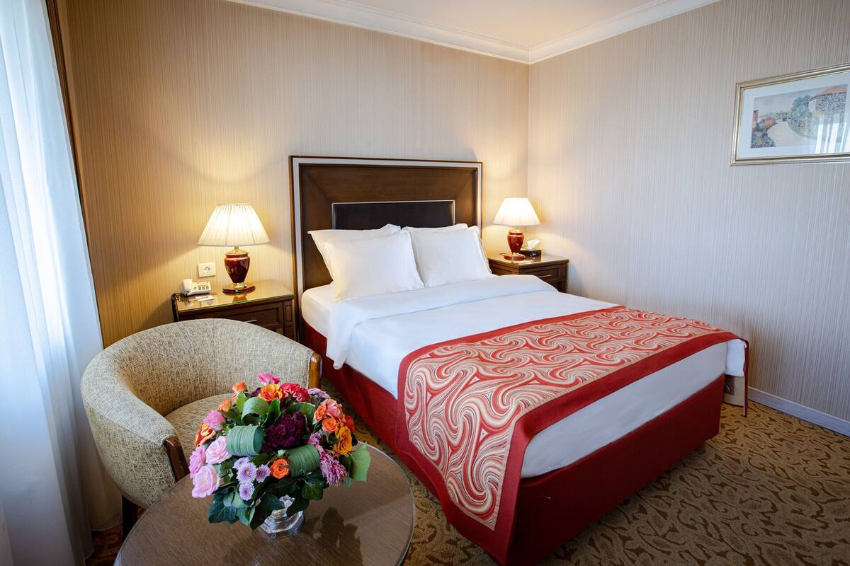Une chambre d’hôtel avec un grand lit, deux tables de chevet avec des lampes, une chaise et un arrangement floral.
