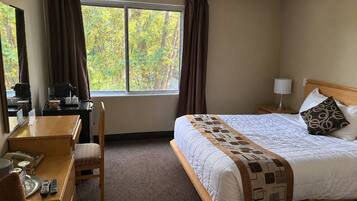 Een hotelkamer met een bed, een bureau, een stoel, een lamp en een raam met gordijnen.