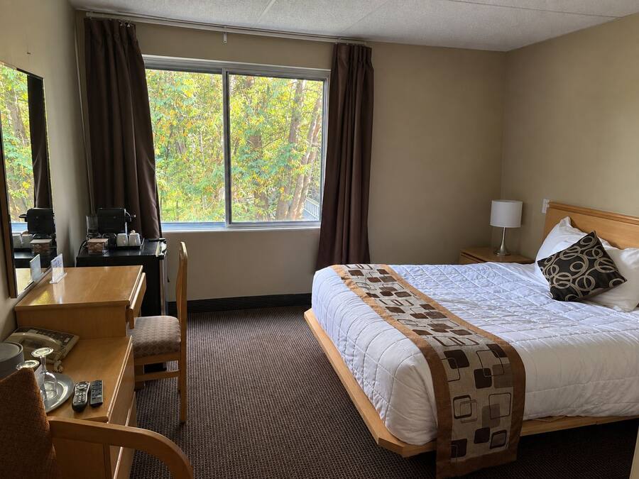 Habitación de hotel con cama, escritorio, silla, lámpara y ventana con cortinas.