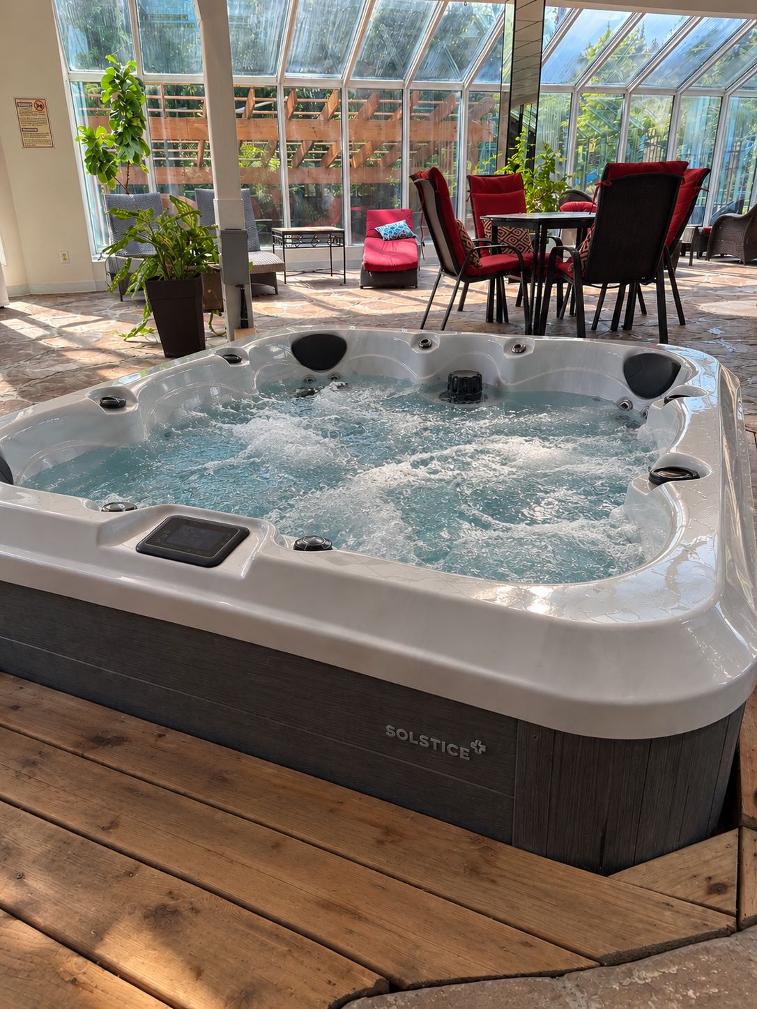 A hot tub with a control panel, surrounded by outdoor seating and a greenhouse structure.