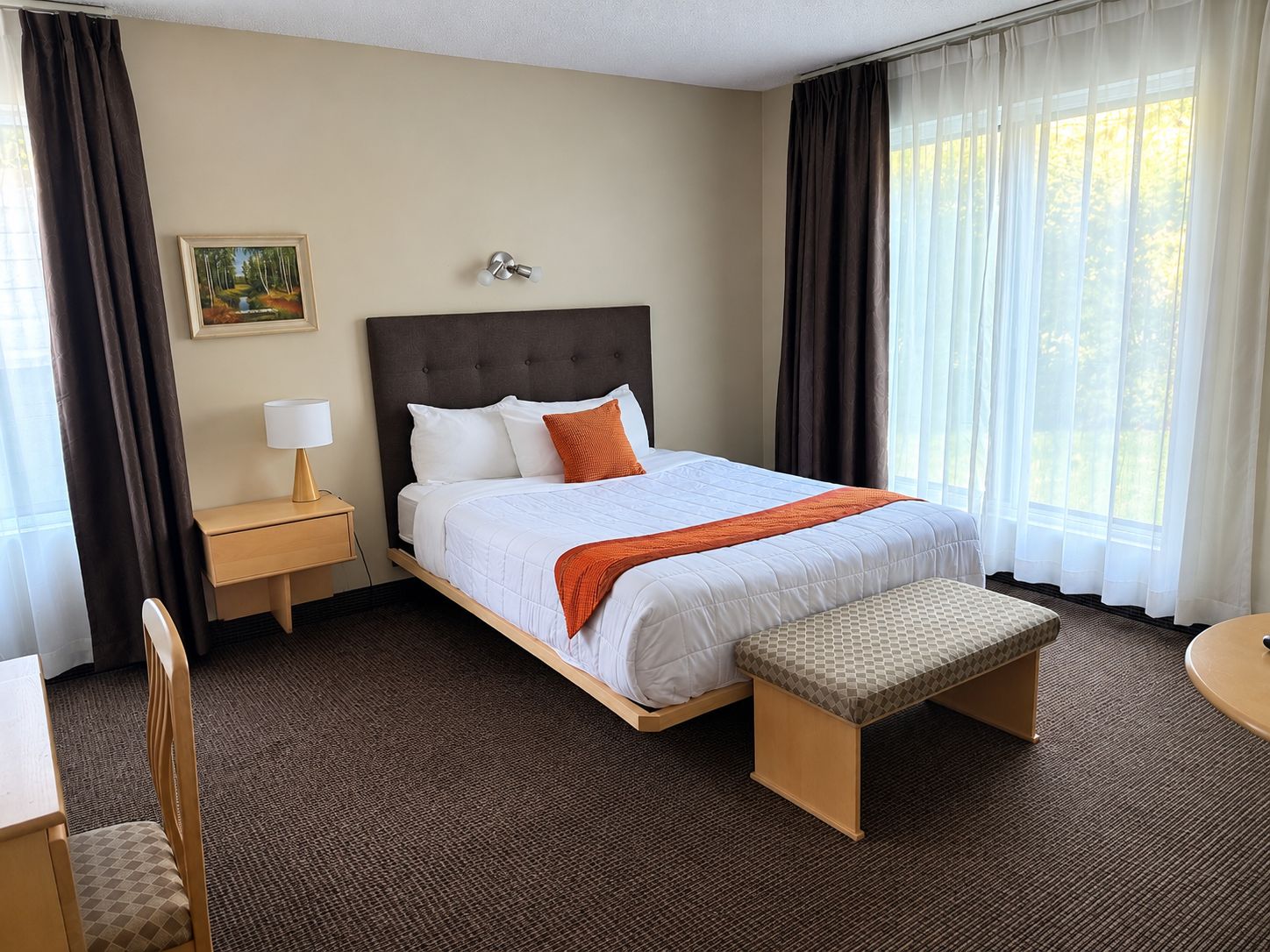 A hotel room with a bed, bedside table, lamp, and a painting on the wall.