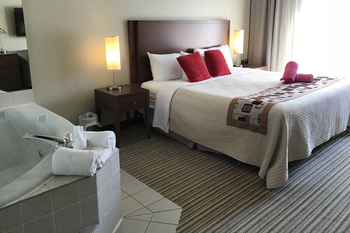 A hotel room with a large bed, a separate bathroom with a bathtub, and two bedside lamps.