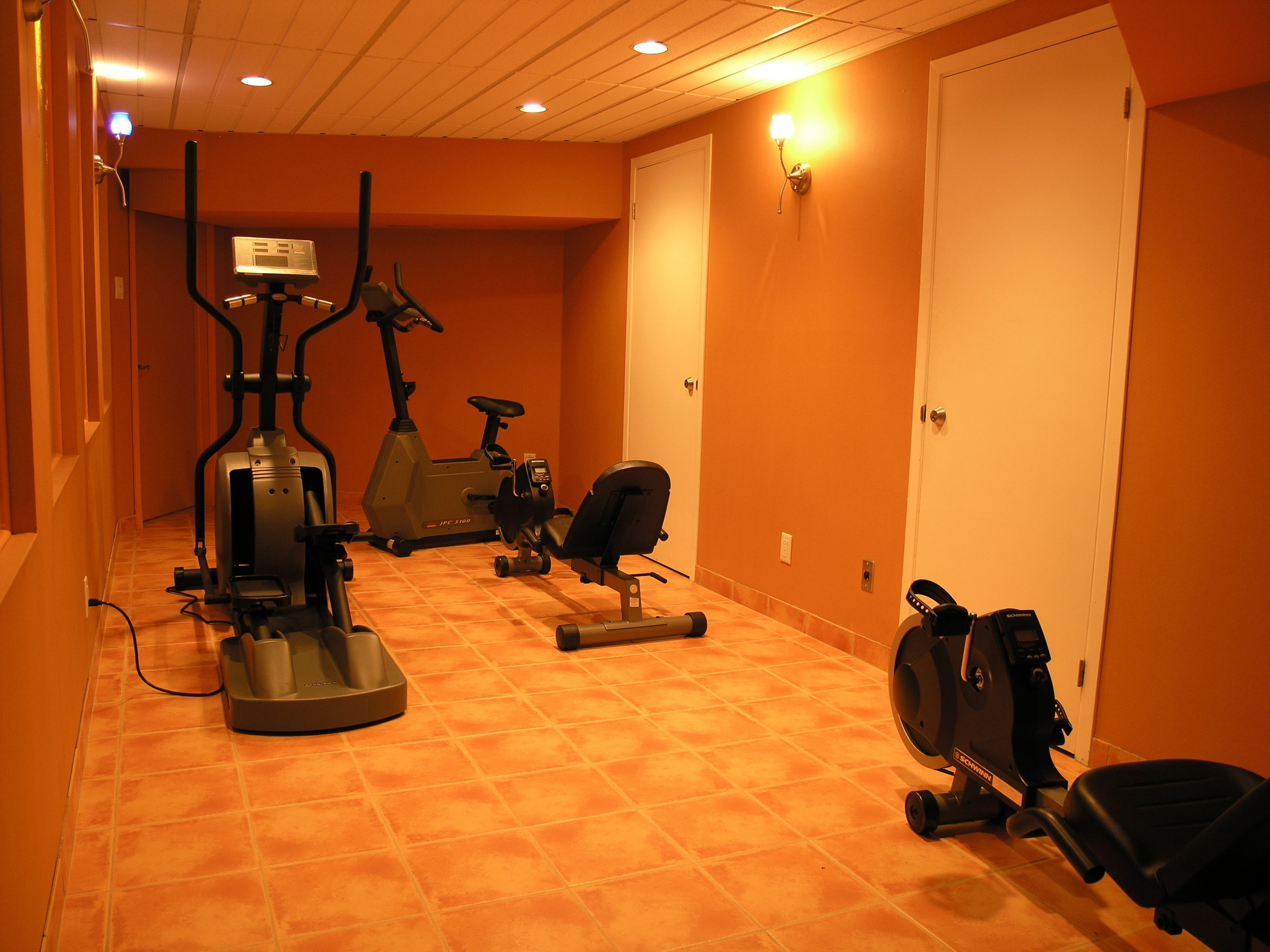 Un gimnasio en casa con equipo de ejercicio, incluyendo una bicicleta estática, una elíptica y una cinta de correr.