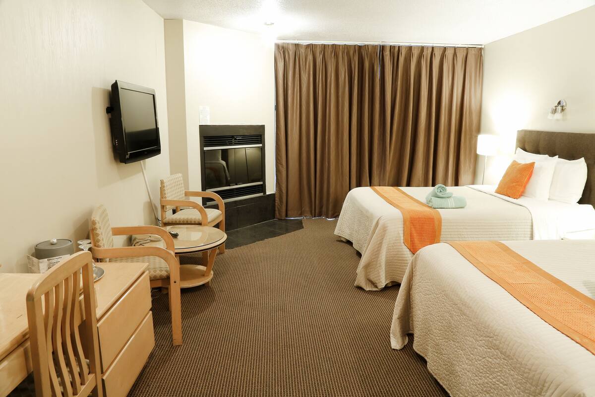 A hotel room with two beds, a TV mounted on the wall, a desk with a chair, and a sofa.