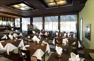 Um restaurante com mesas postas para refeições, grandes janelas e um espaço de bar.