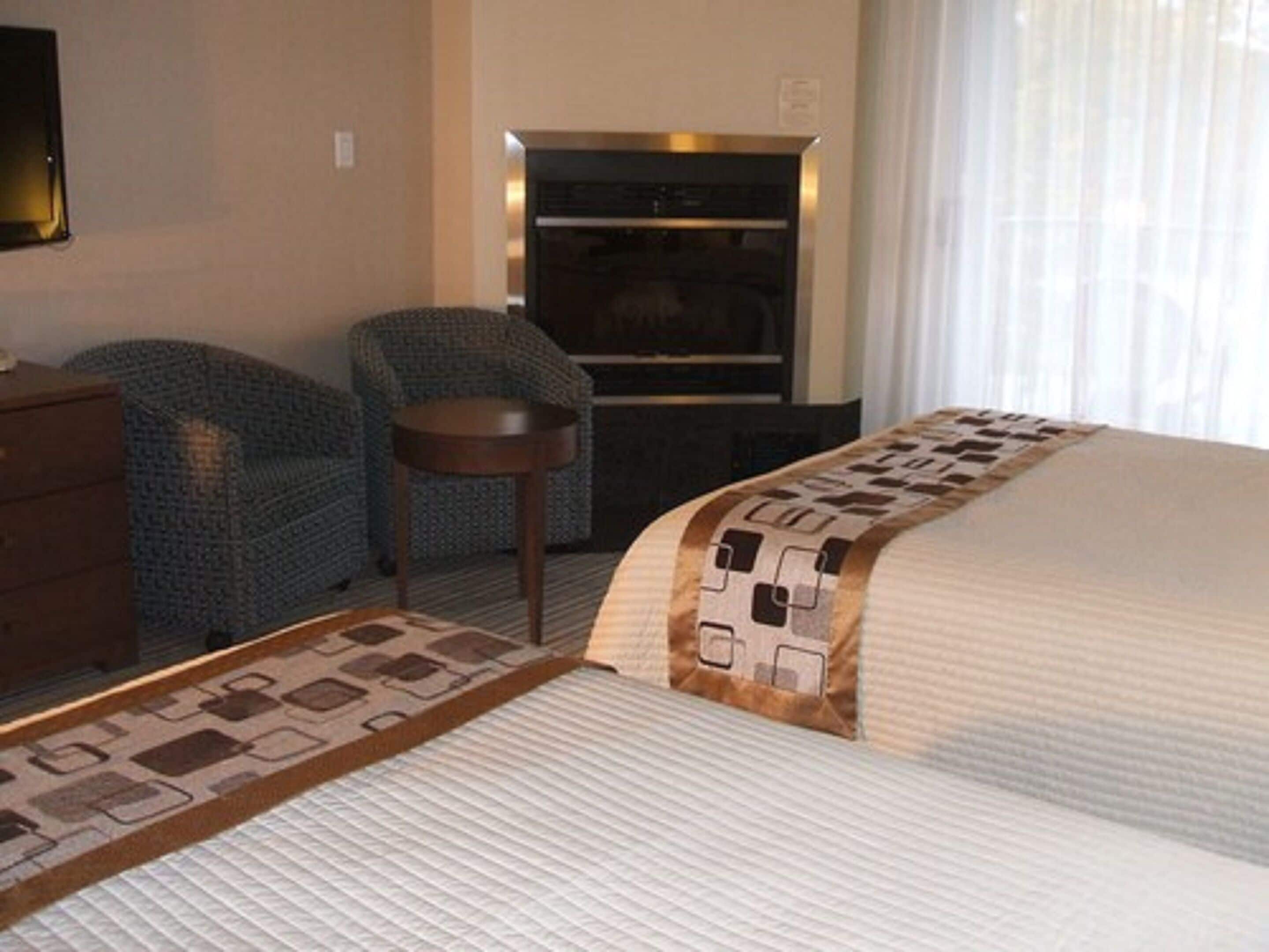 Una habitación de hotel con una cama, un aparador, una silla y una mesita.