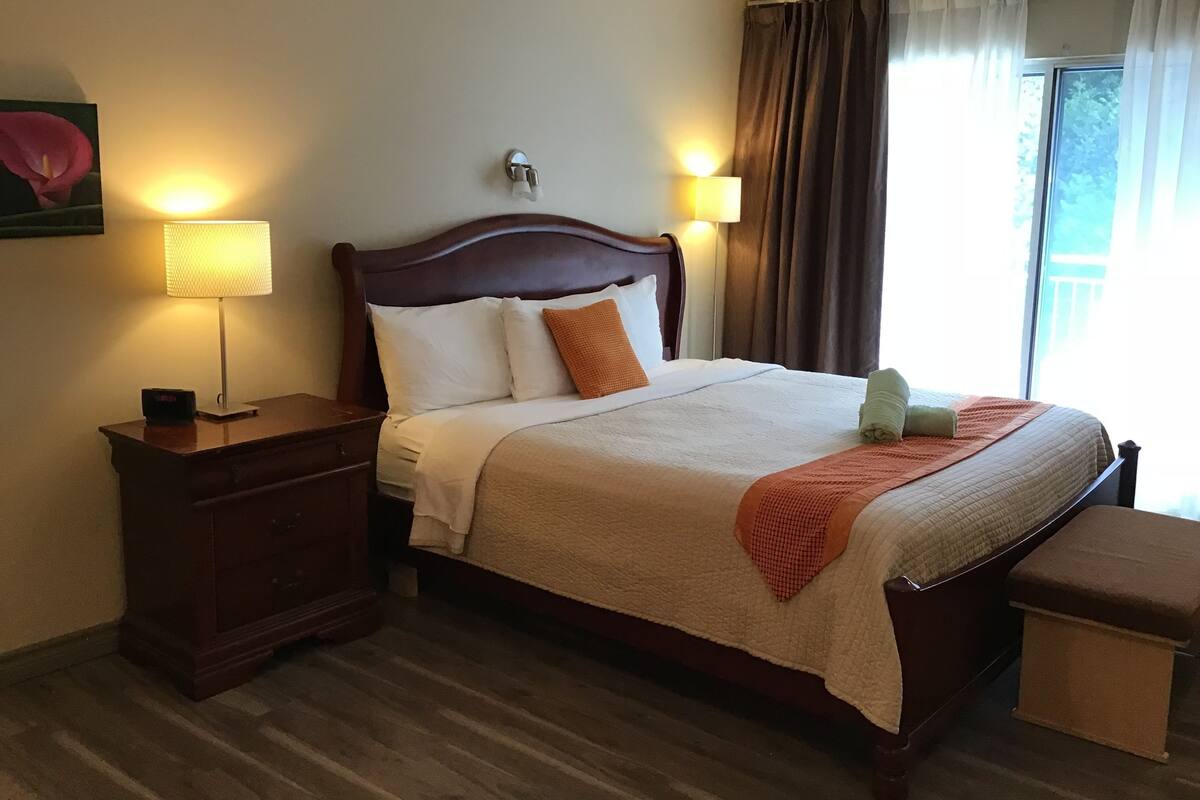 A neatly made bed with a wooden headboard, two bedside lamps, a nightstand, and a window with curtains.