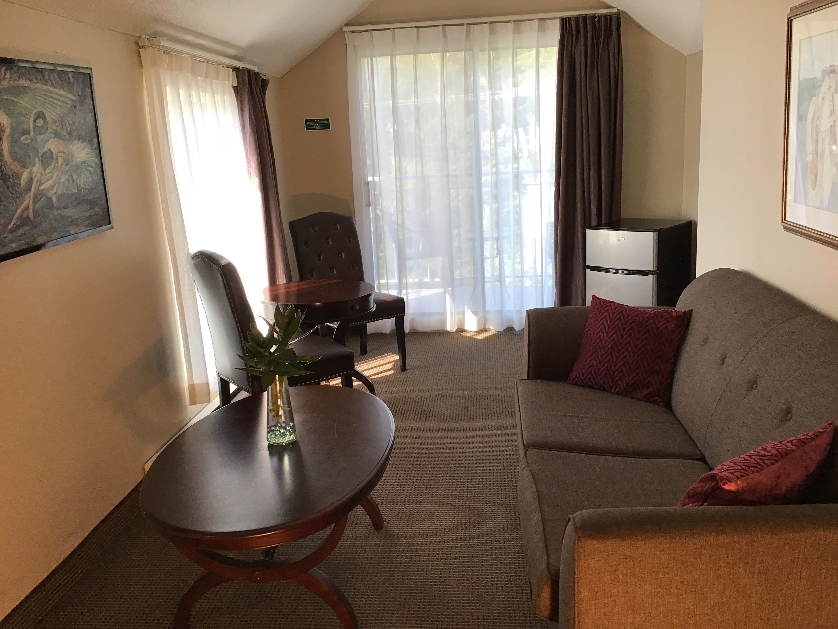 Una habitación de hotel con sofá, una mesa pequeña con un florero, una silla, un escritorio y televisor.