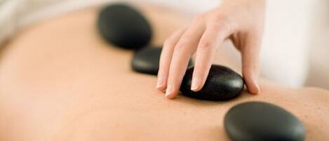 A person receiving a back massage with black stones.