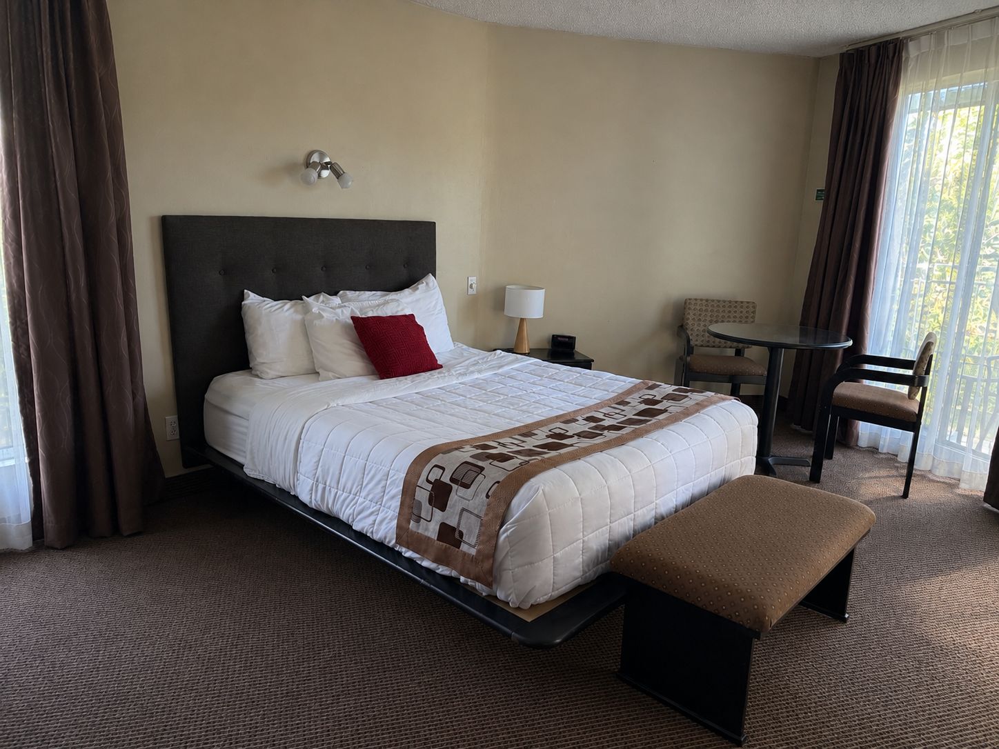 Ein Hotelzimmer mit Bett, Nachttisch, Stuhl und einem Fenster mit Vorhängen.