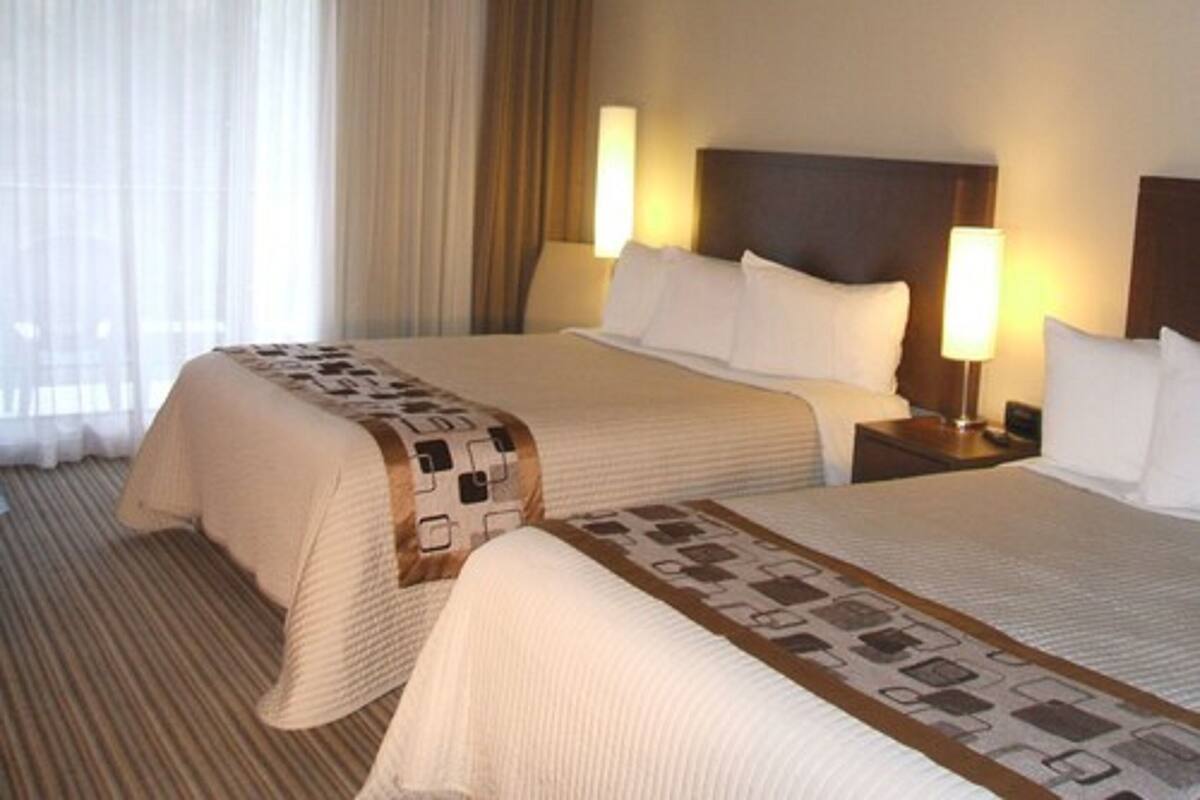 A hotel room with two beds, a large window with curtains, and bedside lamps.