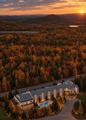 A resort with a swimming pool, multiple buildings, and a forested backdrop. - Hôtel Spa Excelsior (Sainte-Adele)