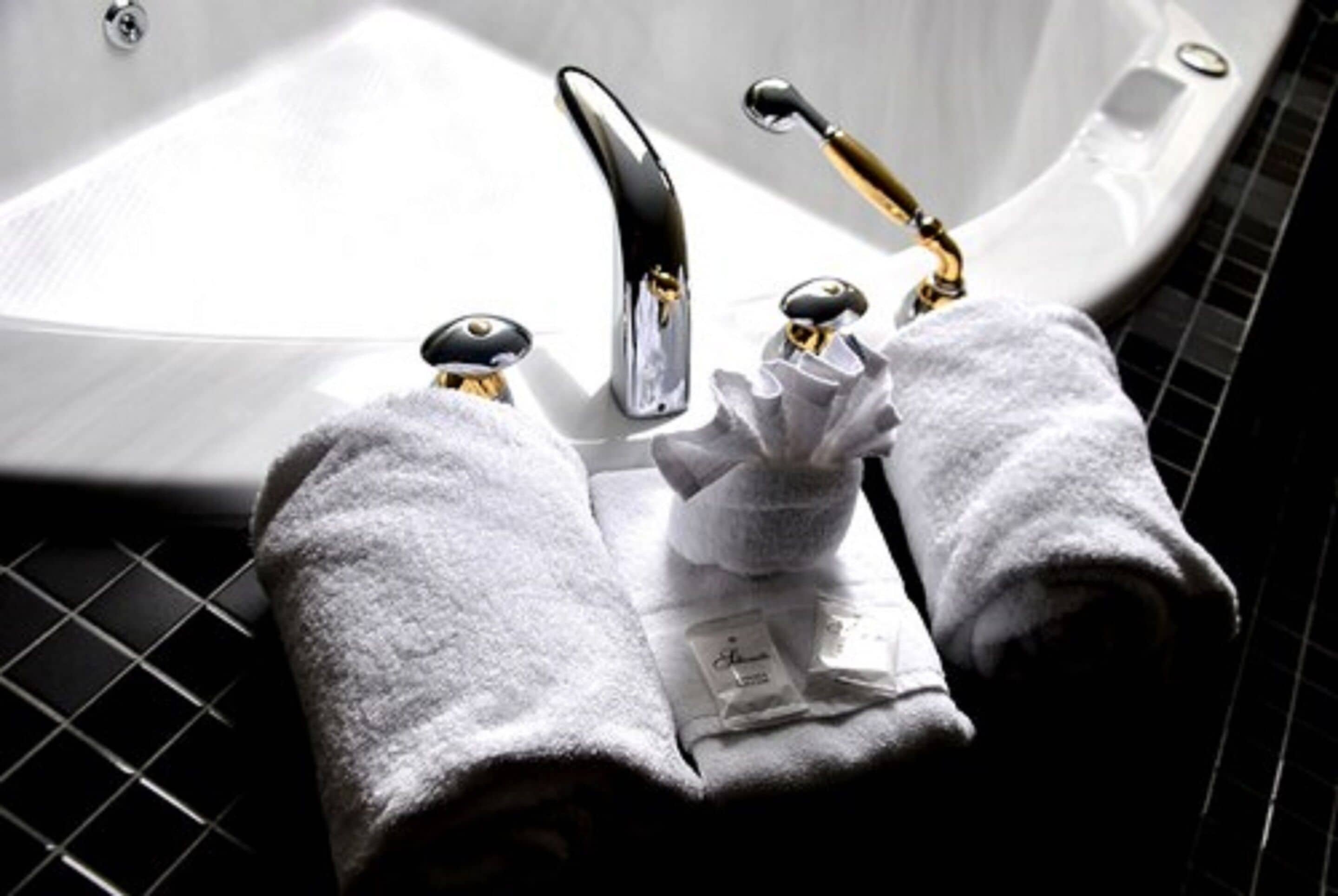 A bathroom with a white bathtub, two gold faucets, and two white towels on a black tiled floor.