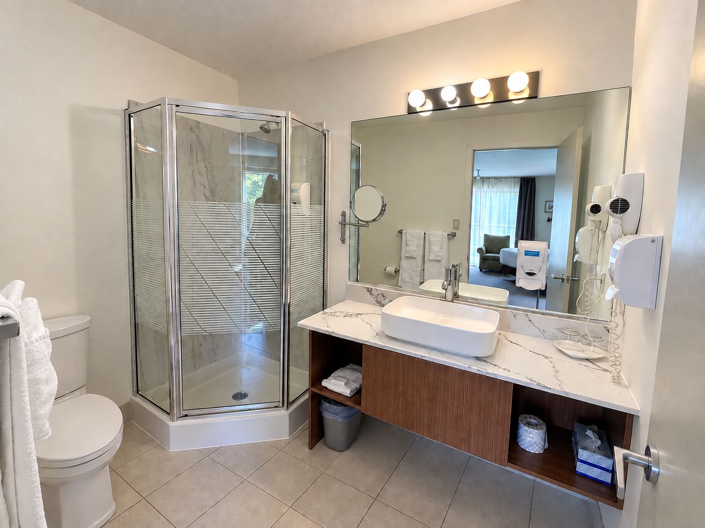 Un baño moderno con ducha envuelta en vidrio, tocador con lavamanos y un espejo grande.
