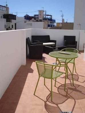 A rooftop terrace with outdoor seating, including a sofa and two round tables with chairs.