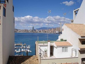 A coastal cityscape with a marina, buildings with tiled roofs, and a clear sky.