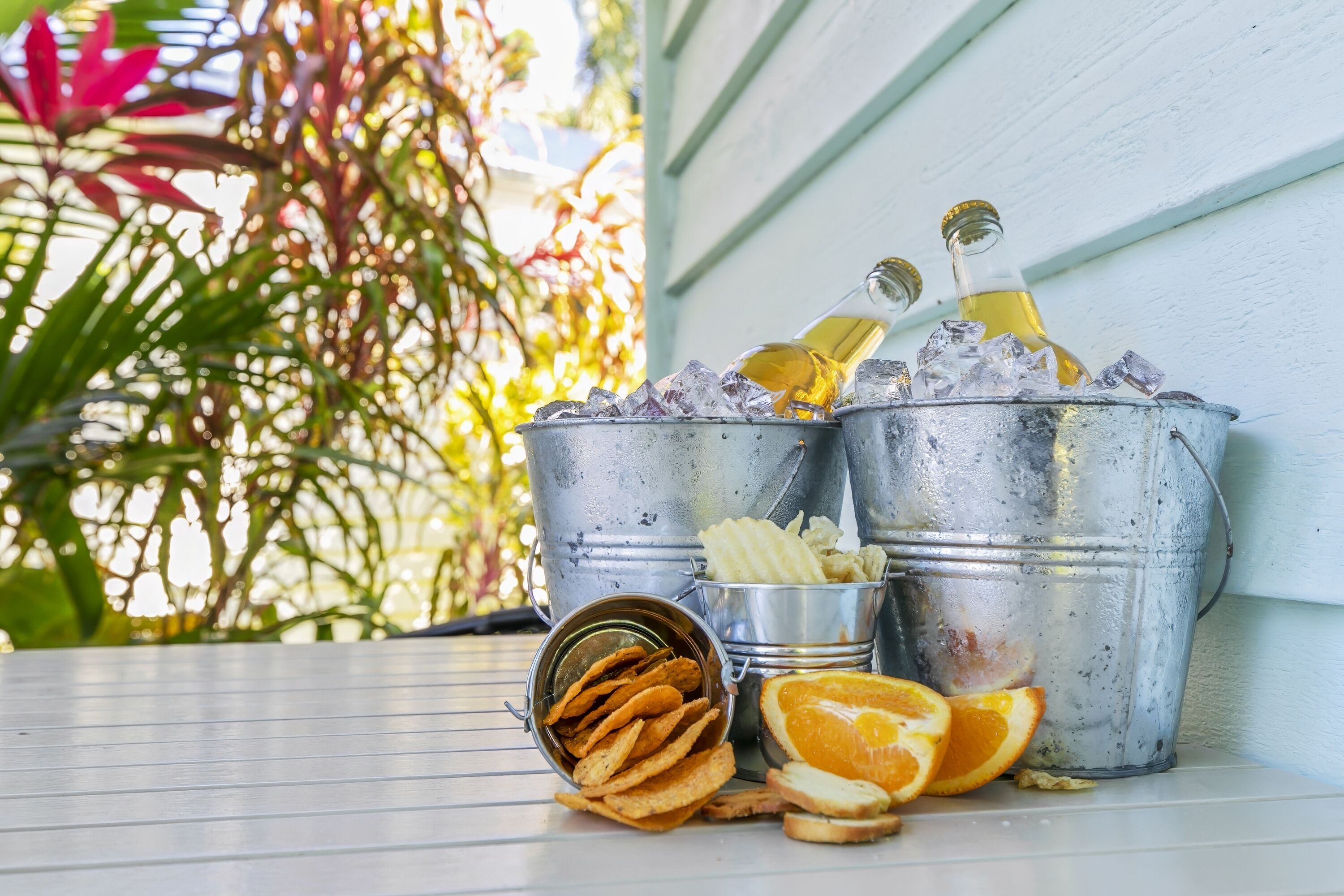 Two metal buckets with ice and a bottle of yellow liquid, a tin of crackers, and orange slices on a table.