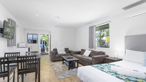 Ein modernes Hotelzimmer mit einem Bett, einem Sofa, einem Esstisch mit Stühlen und einer kleinen Küchenzeile.