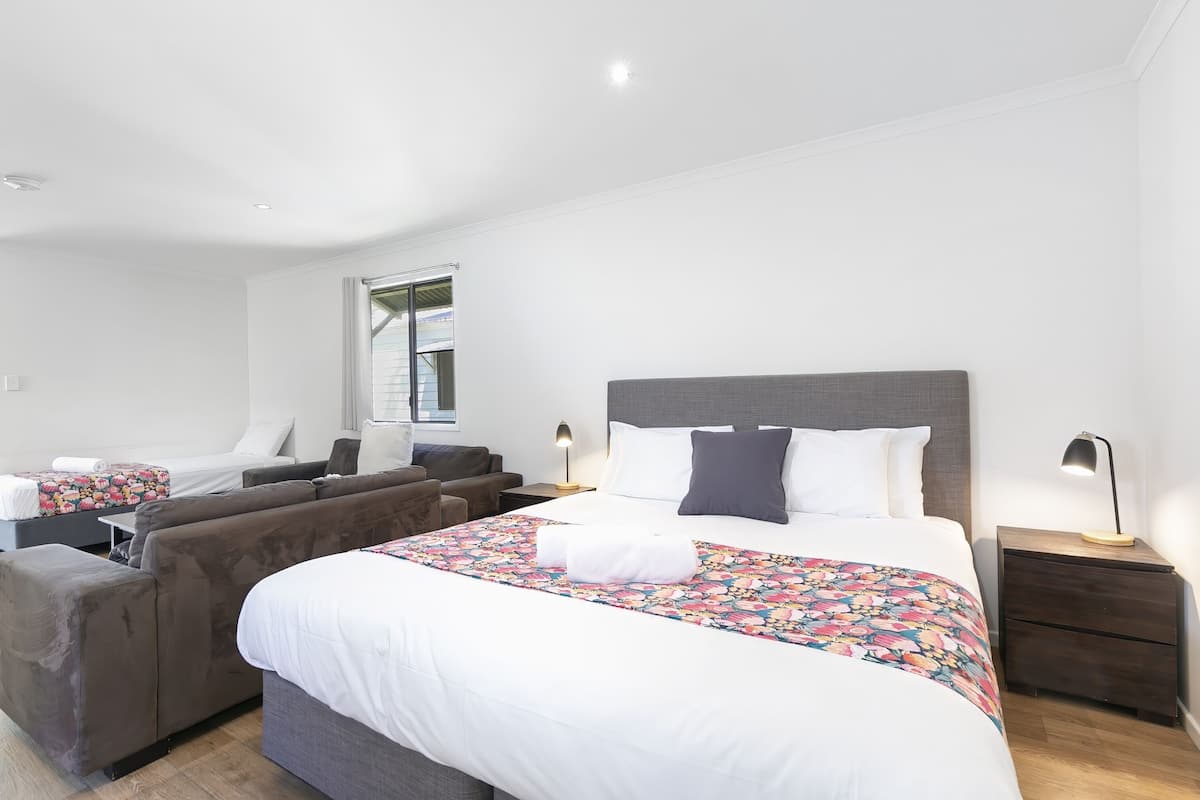 A modern hotel room with a large bed, a sofa, a desk, and a nightstand.